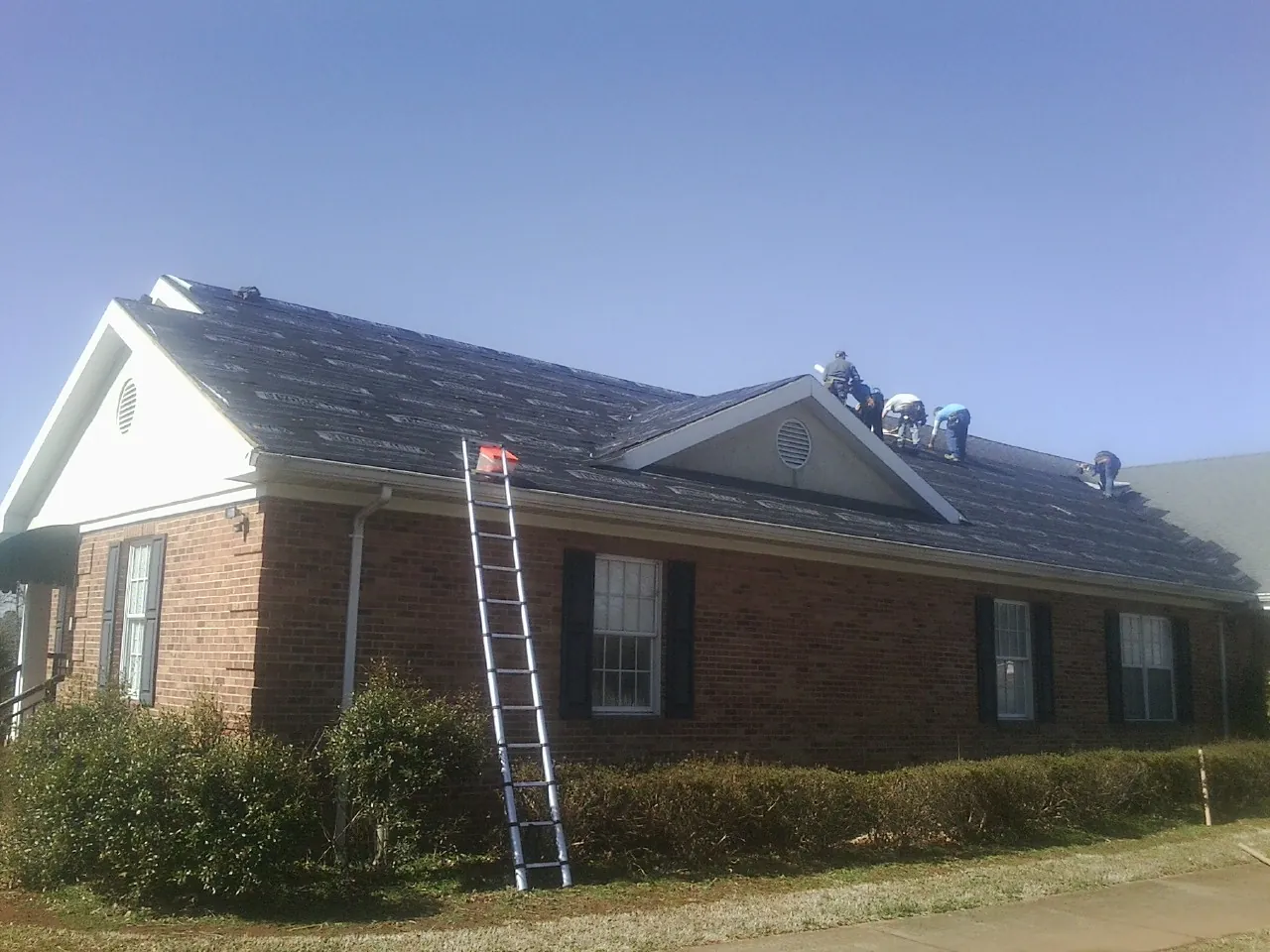 Crew tearing shingles off a brick ranch roof with a ladder set — Emergency Roof Repair work by our crew in Pitman