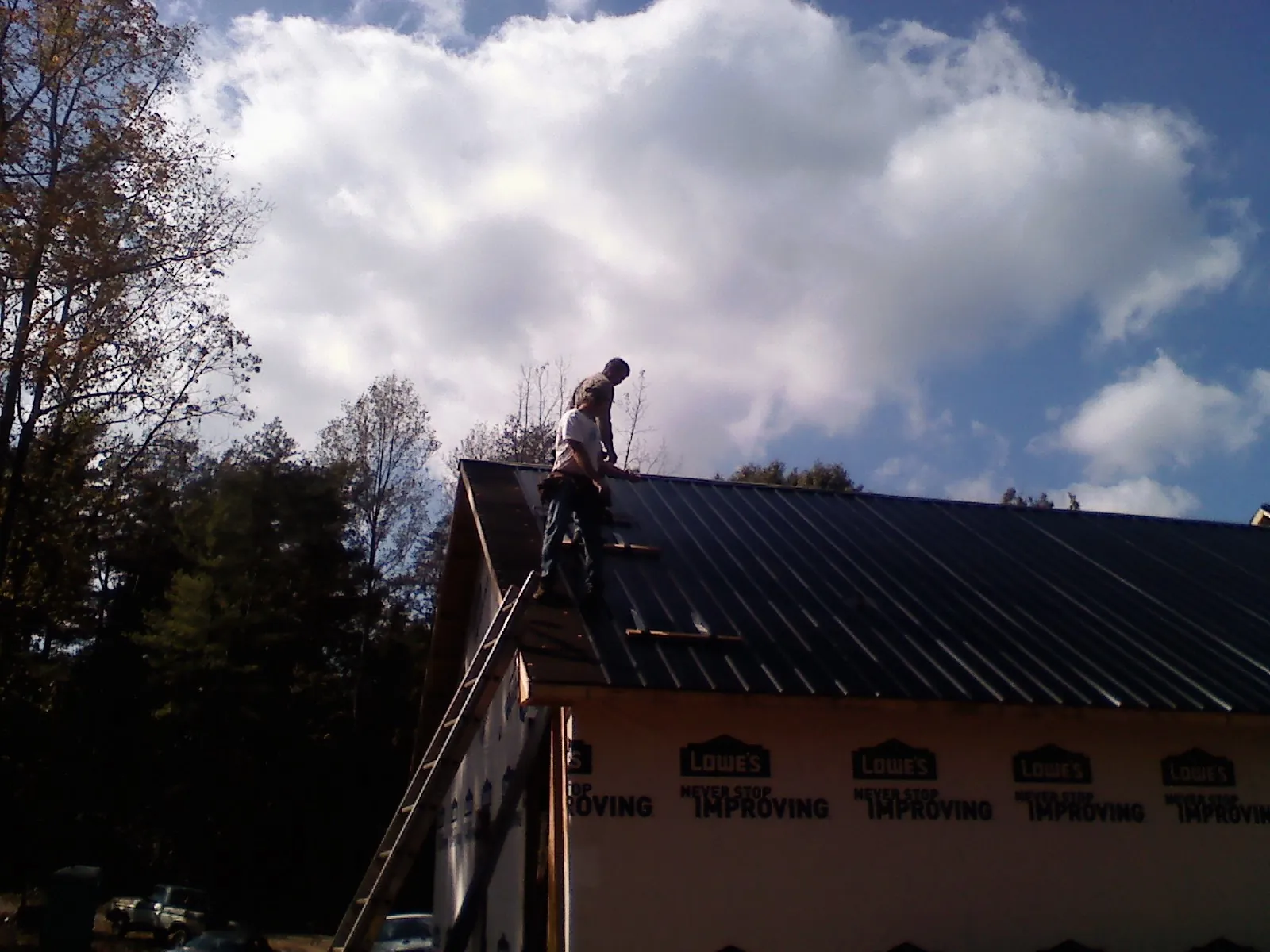 Roofer fastening dark metal panels high against a cloudy sky, from a Roof Inspection job in Pitman