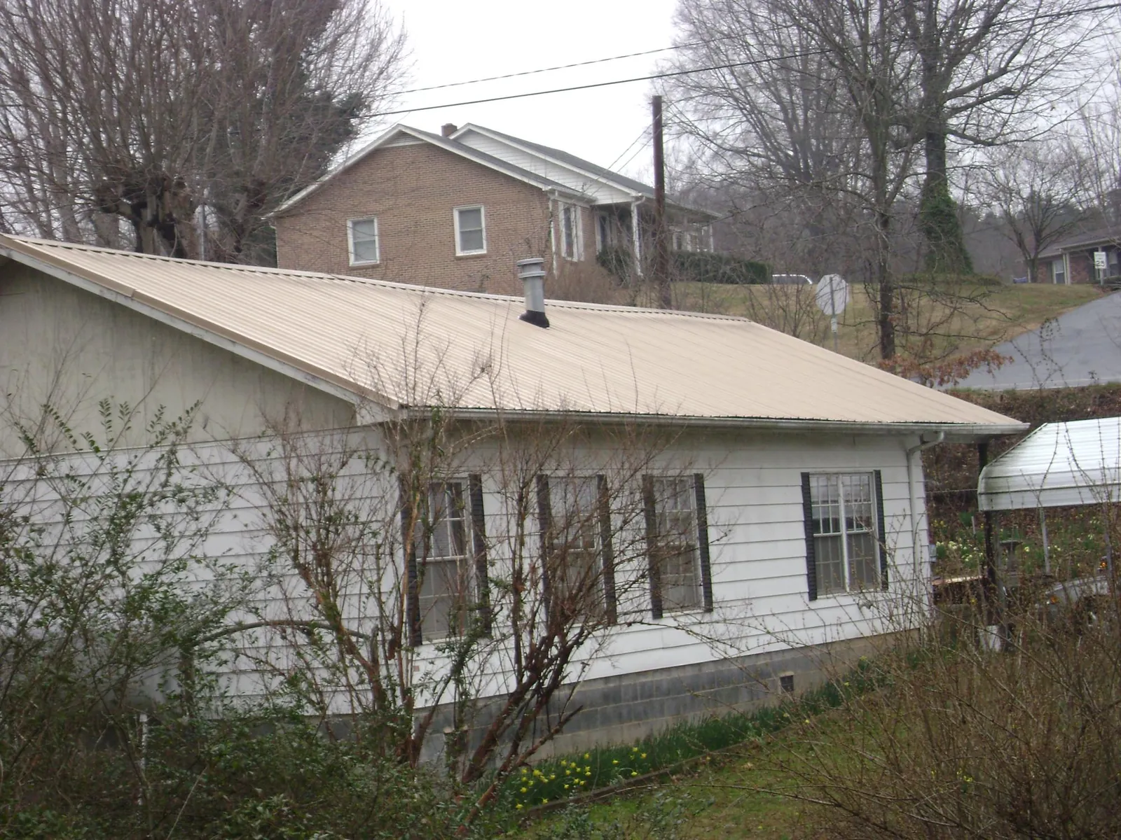 Tan metal roof on a white sided house set into a hillside — Commercial Roofing by Roofing Brothers in Pitman